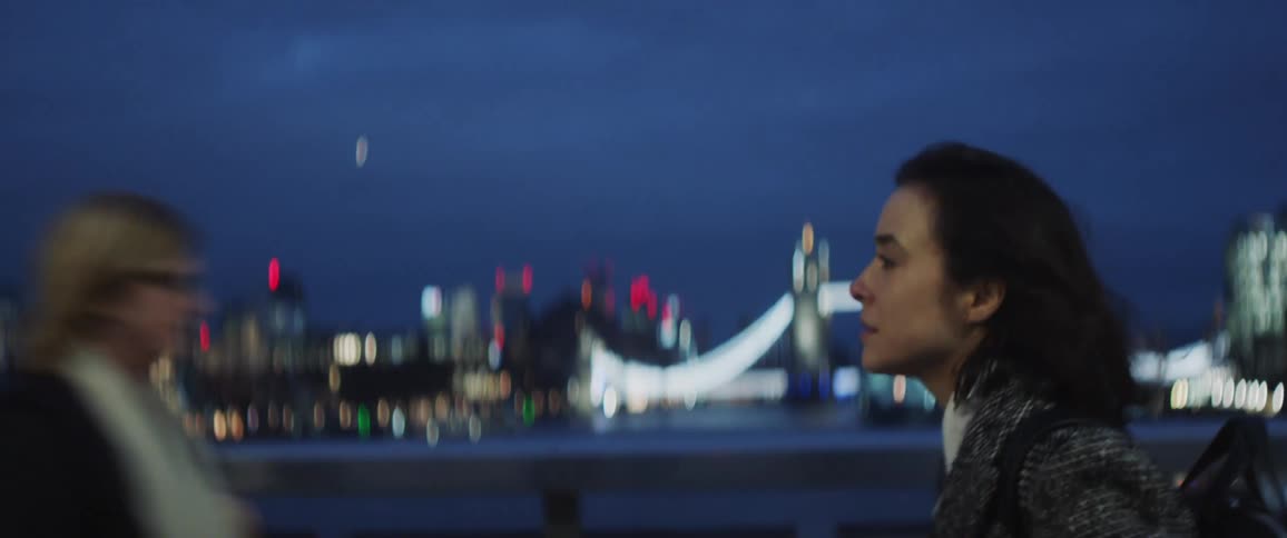 Woman with gray jacket and black backpack walks across the bridge