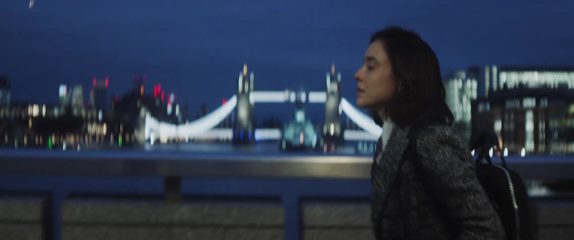A woman looking sad and tired walks through a busy london bridge at night