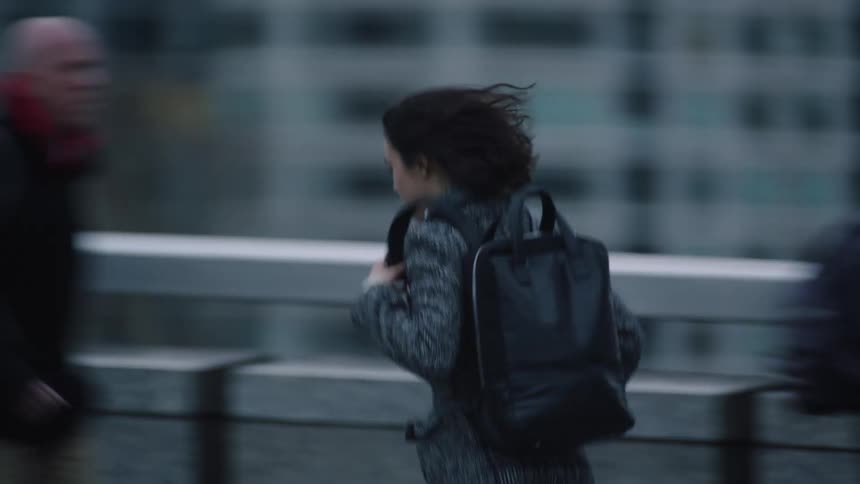 Woman wearing backpack rushes along busy sidewalk on bridge