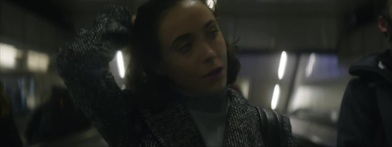 A woman looking sad and tired runs her hand through her hair as she goes down an escalator