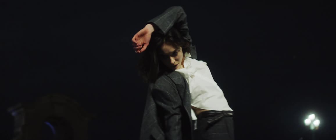 Woman with white top and gray jacket dances on the bridge at night