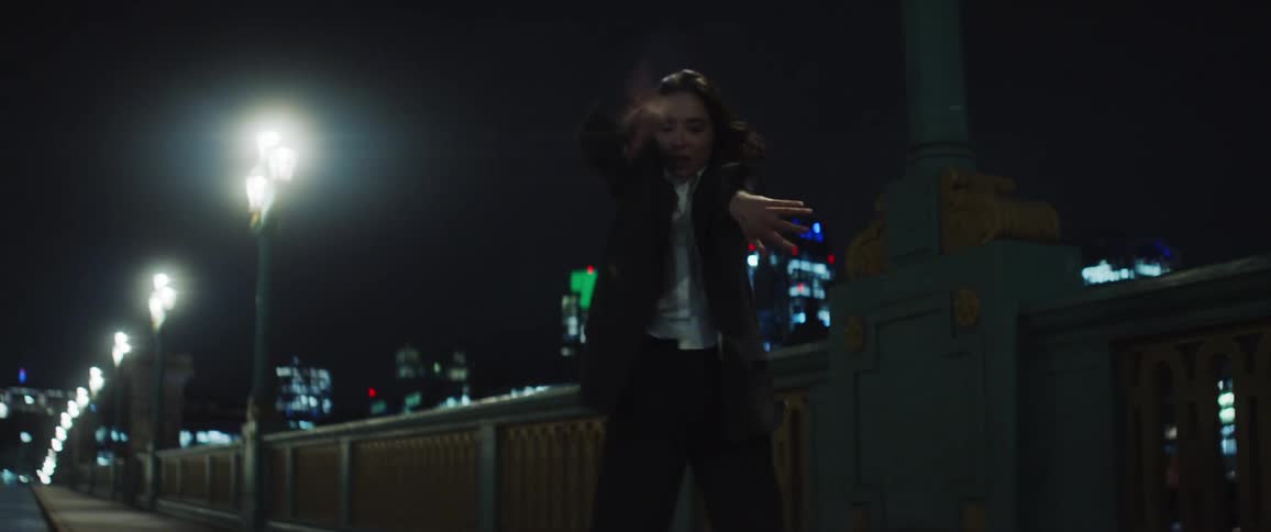 A woman dancing erratically on a bridge sidewalk as street lights light up the road