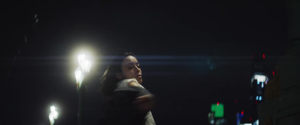 Woman dances near bridge rail at night with city skyline in the background