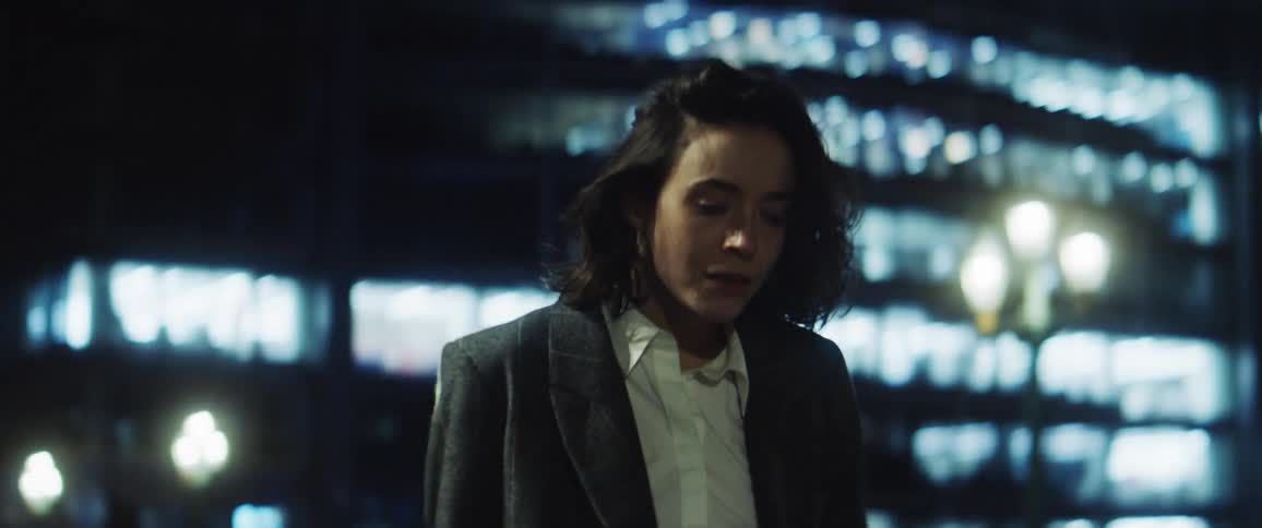 A young woman walks down an urban street at night and then collapses