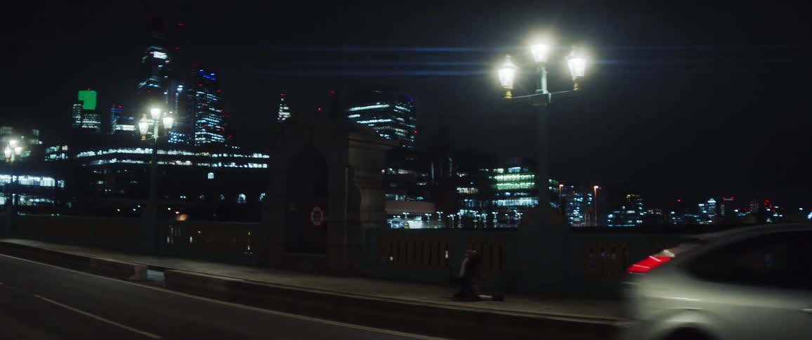 A person dancing on a sidewalk as cars pass by and the city buildings are lit up in the distance