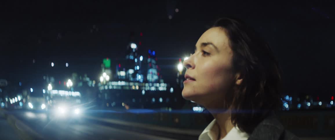 Female dancer dances on the bridge against the illuminated high rise buildings in the background at night