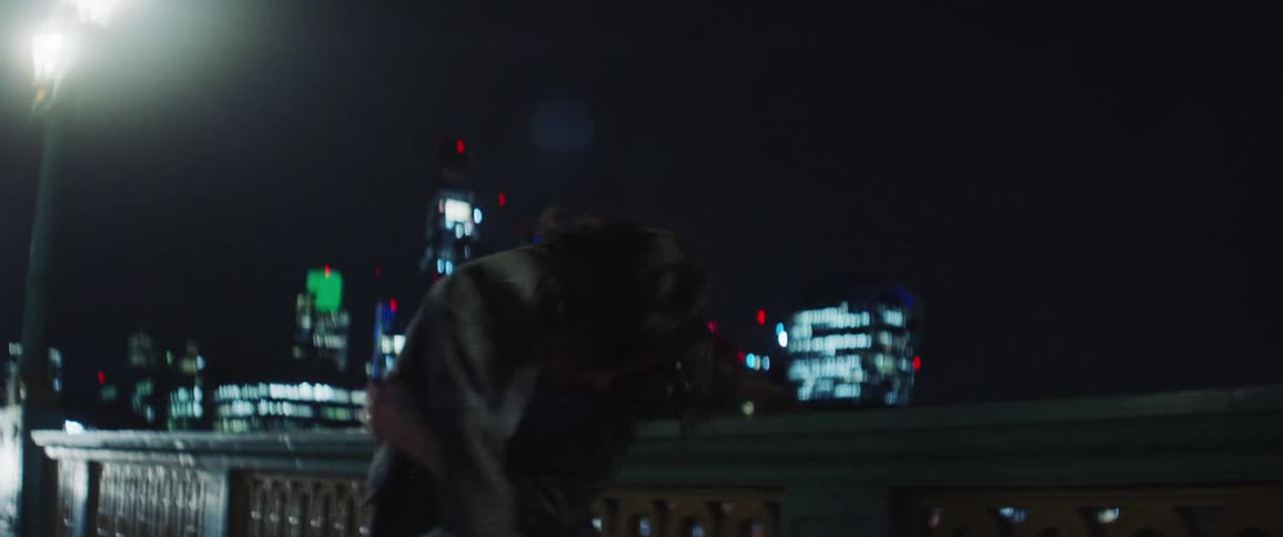 Woman with gray blazer jacket and black pants dances on bridge against the city skyline at night
