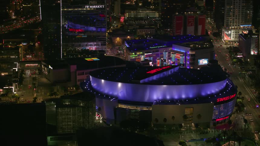 Drone view of a round stadium lit up at night in a dense city