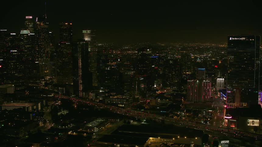 Heavy traffic flows along highway between downtown skyscrapers at night