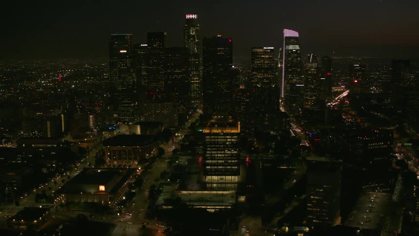 Traffic moves on downtown streets as towers and skyscrapers overlook the city with their lights glowing in the darkness