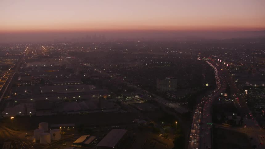 Heavy traffic flows along roads through dark cityscape under a red horizon