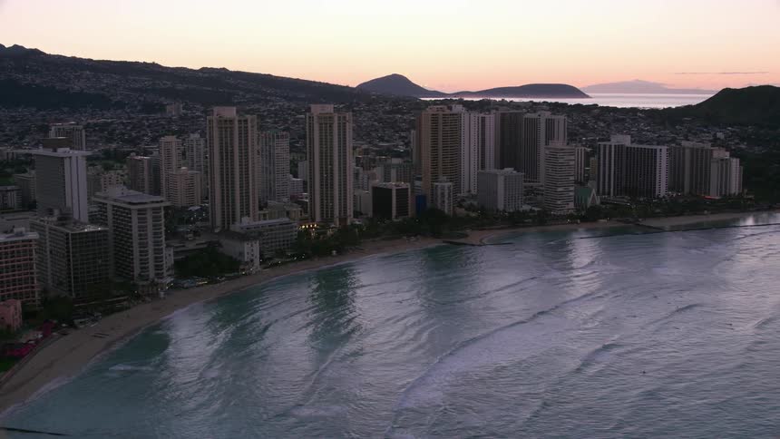 High rises hug beach on edge of small city stretching up mountain against a red tinted horizon