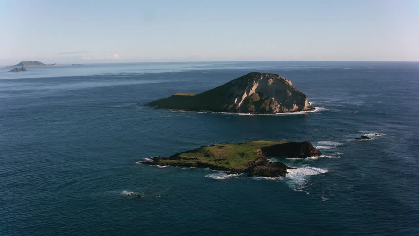 An aerial of the ocean landscape with land formations as waves crash against the rocks