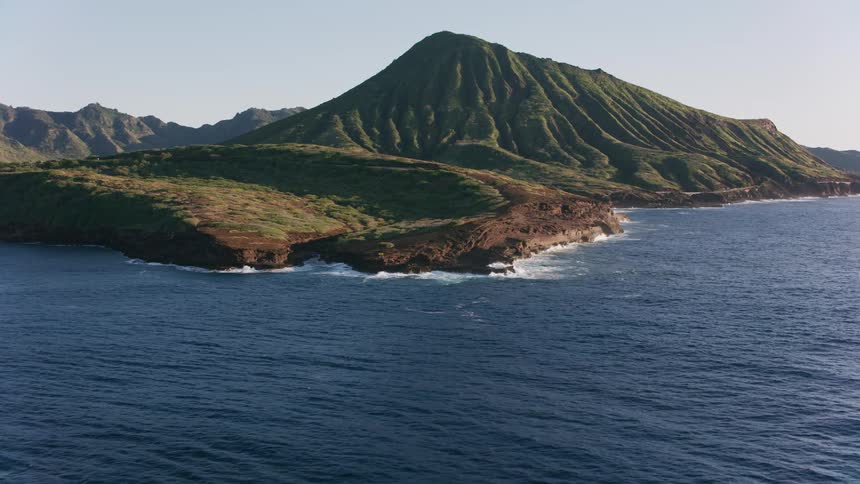 Waves crash against rocky shore near hills and mountains