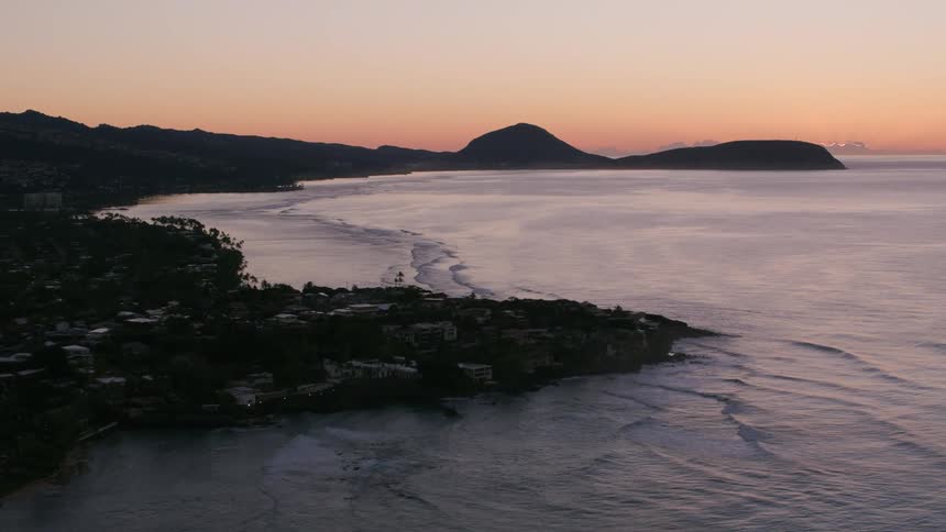 Drone view of the ocean waves rolling onto the coast land as the sun is rising