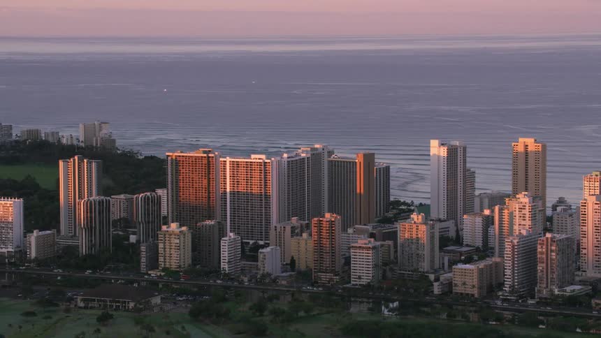 An aerial of a coastal city with tall buildings along the beach and a park behind the buildings