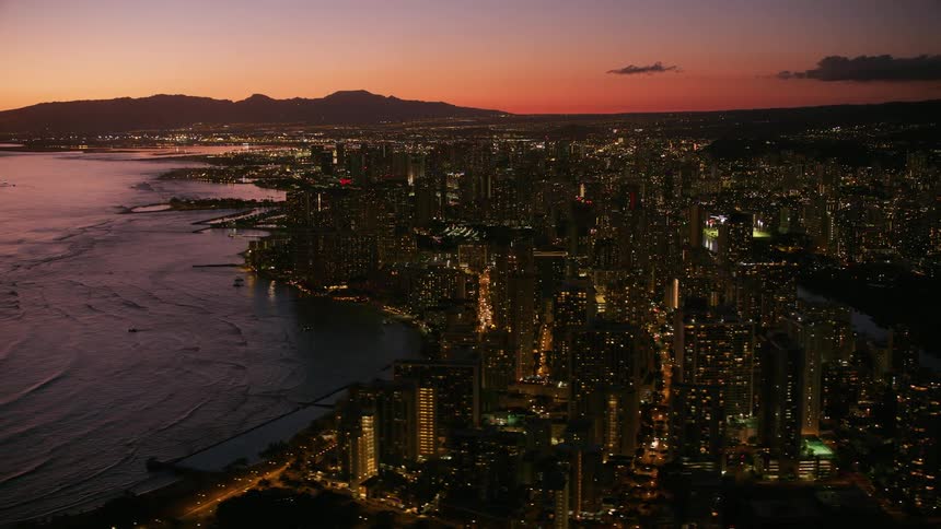 A coastal city at dusk with a river at its center the ocean on one side and a mountain range in the background