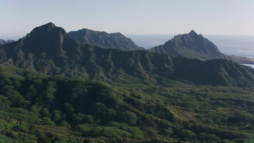 An aerial view of a mountain range covered in vegetation with the sea behind it
