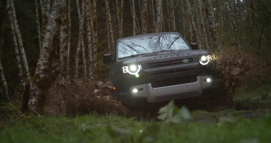 An suv drives through a puddle in a forest splashing mud around