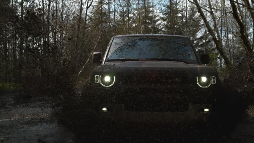 An suv in a forest drives through a mud puddle splashing it around