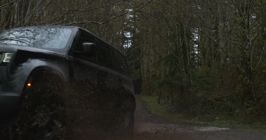 An suv drives through a mud puddle in a forest splashing mud all around