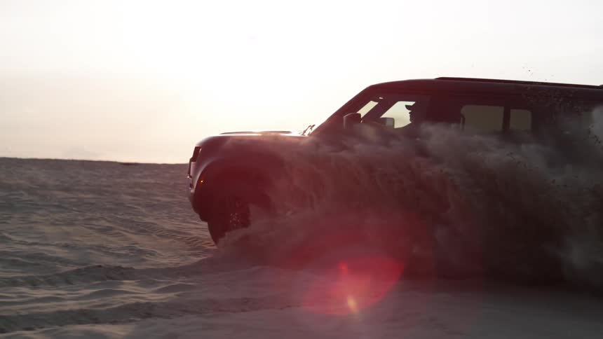 An suv driving through a dessert spreading sand around as it passes