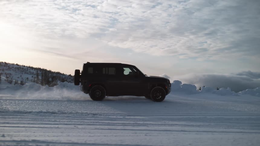 A black truck is traveling on a snow covered road with snow covered mountains in the distance