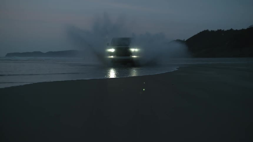 Black land rover defender drives along the beach at dusk