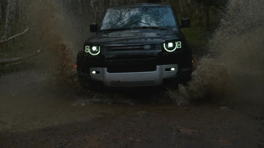 An suv drives through a small shallow pond in a forest splashing water all around