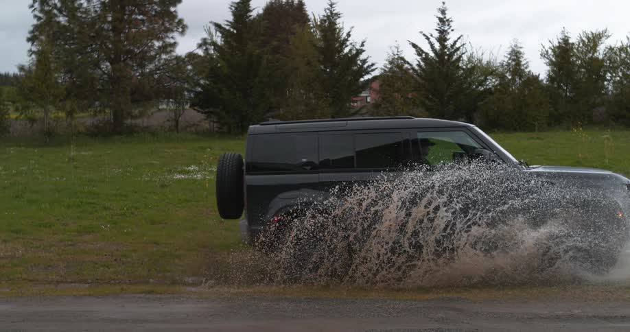 Black suv car driving on dirt road splashing water in the field