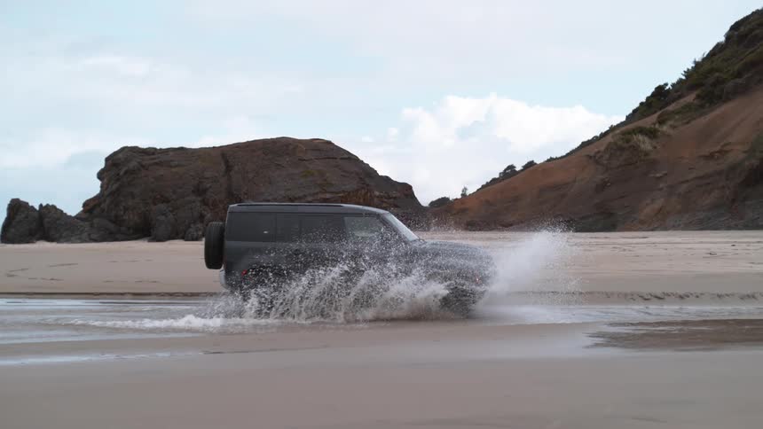 A vehicle drives through shallow water on the beach