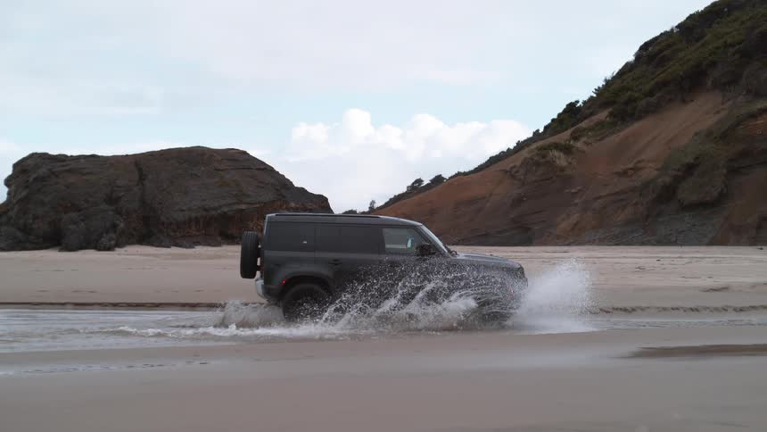 Jeep drives through water on beach splashing water into air