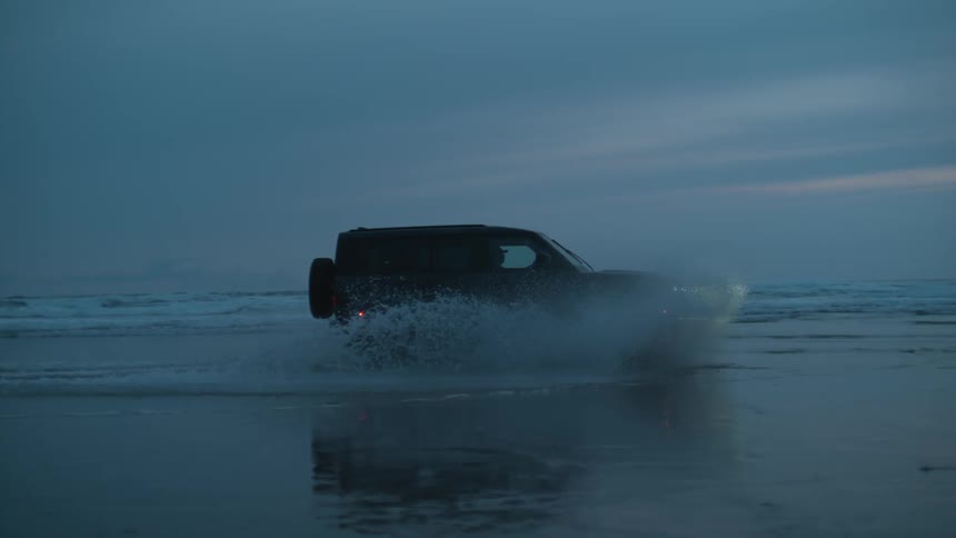 The vehicle is driving through the water on the beach
