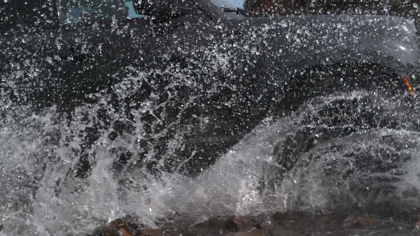 Vehicle splashes water into the air as it drives through water on beach