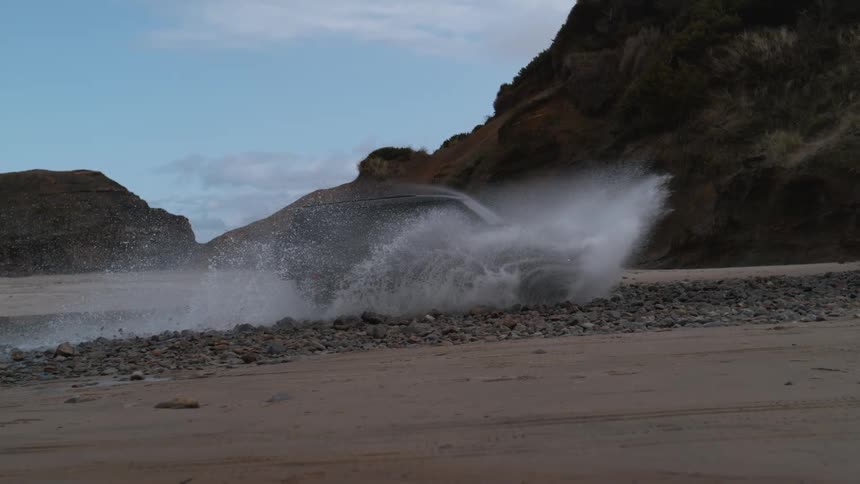 Black land rover defender drives on the beach