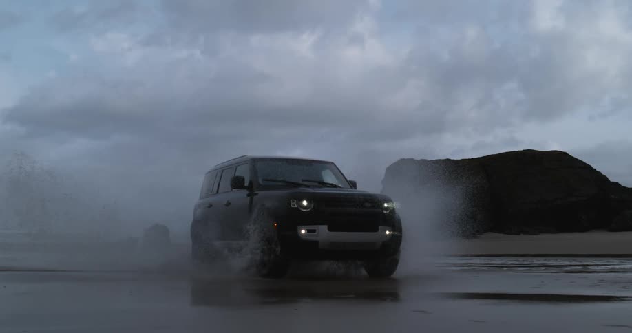 A vehicle drives through shallow water on the beach