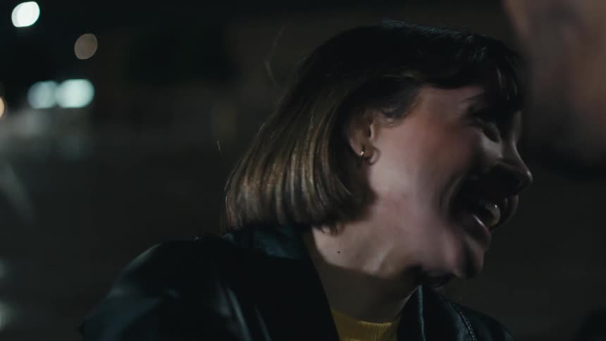 Woman with leather jacket and brown hair looks at man laughing