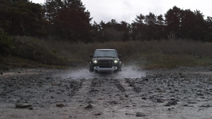 A car in a watery land trying to travel through the land with trees at the back of the land