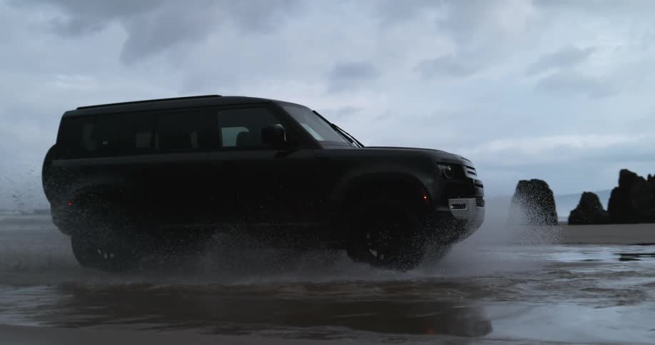 An suv drives across shallow water on a beach splashing it around