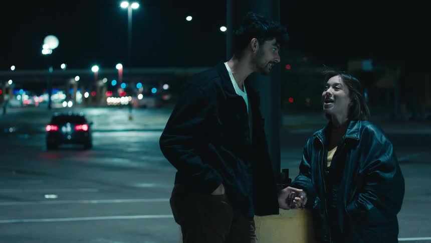 Man in black jacket and woman wearing leather jacket talks with each other on the street at night