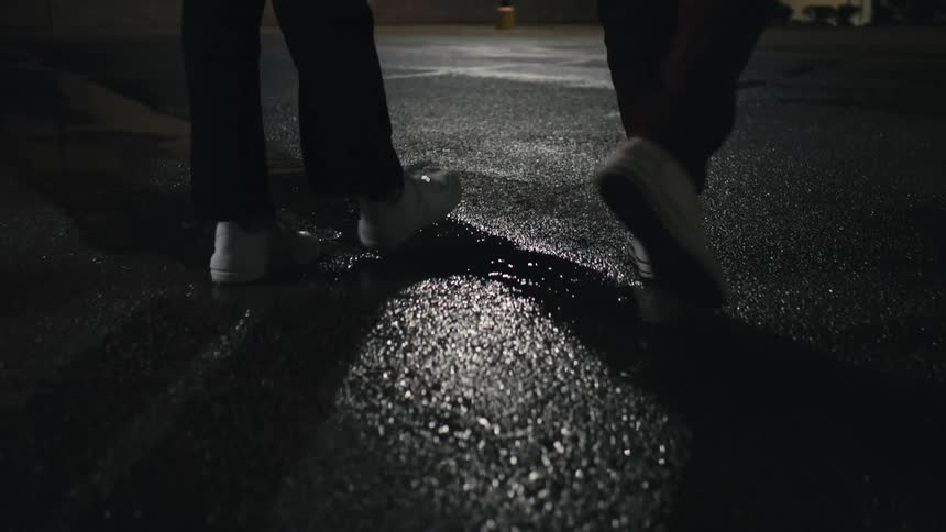 Man and woman wearing black pants and white shoes walk down the street at night