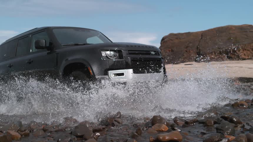 A sport utility vehicle drives over rocks in the ocean