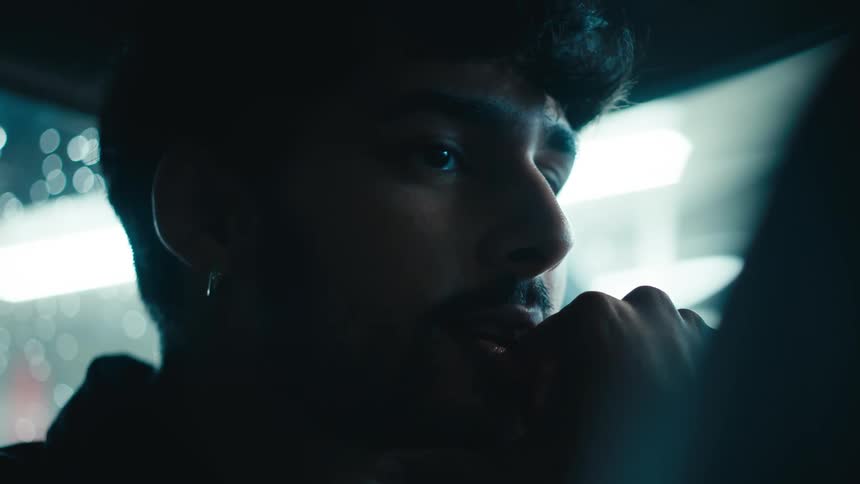 A young man inside a car touches his beard as he listens intently to someone then nods and smiles