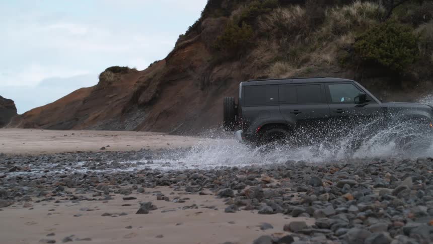 A black truck splashes as it travels through a water puddle on a stone road near a mountainside