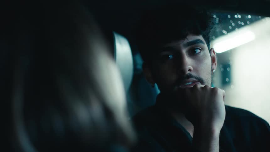 A man and a woman talk inside the car and the man listens attentively