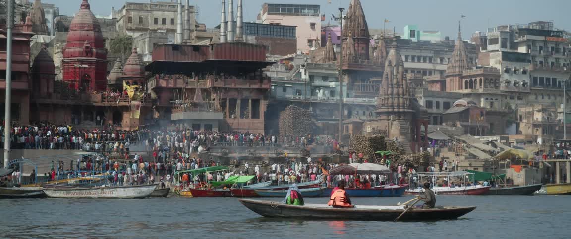 People on boats and people on waterfront near historic traditionally architected buildings stand watching