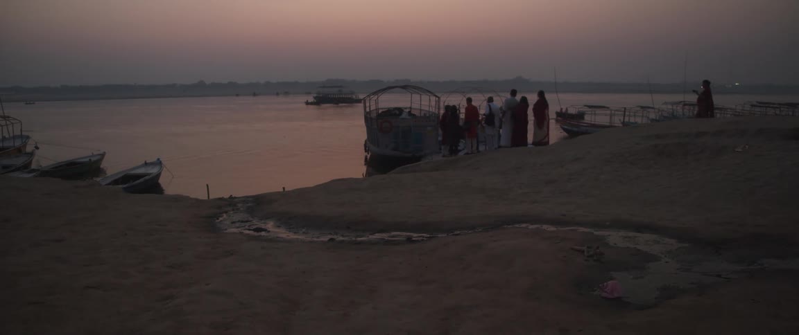 A group of people wait near a boat at dusk
