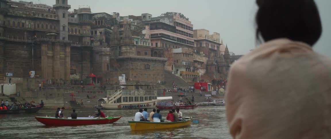 Woman watches people rowing down river with historic buildings in the background