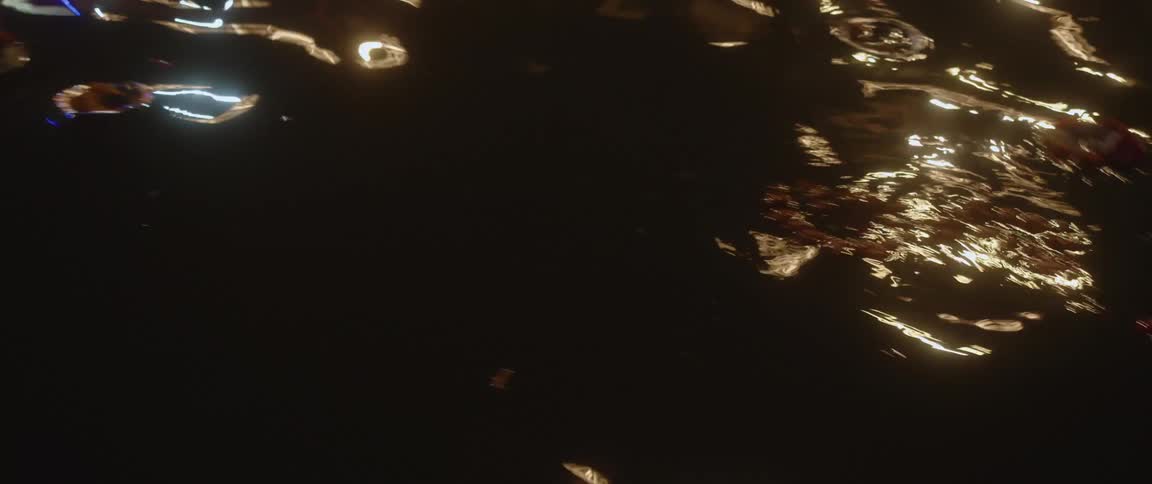 Light reflects on the water in the darkness and candles on tins and vegetables float on the surface