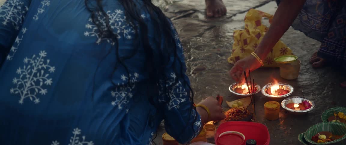 Two women kneeling on the floor light candles and incense in bowls